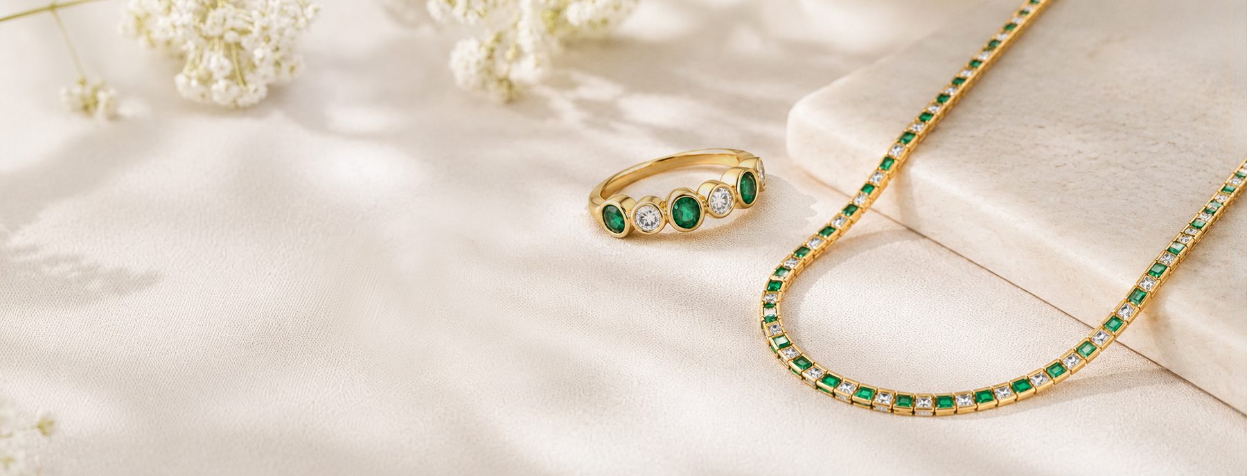 Emerald and diamond ring beside a tennis necklace on stone